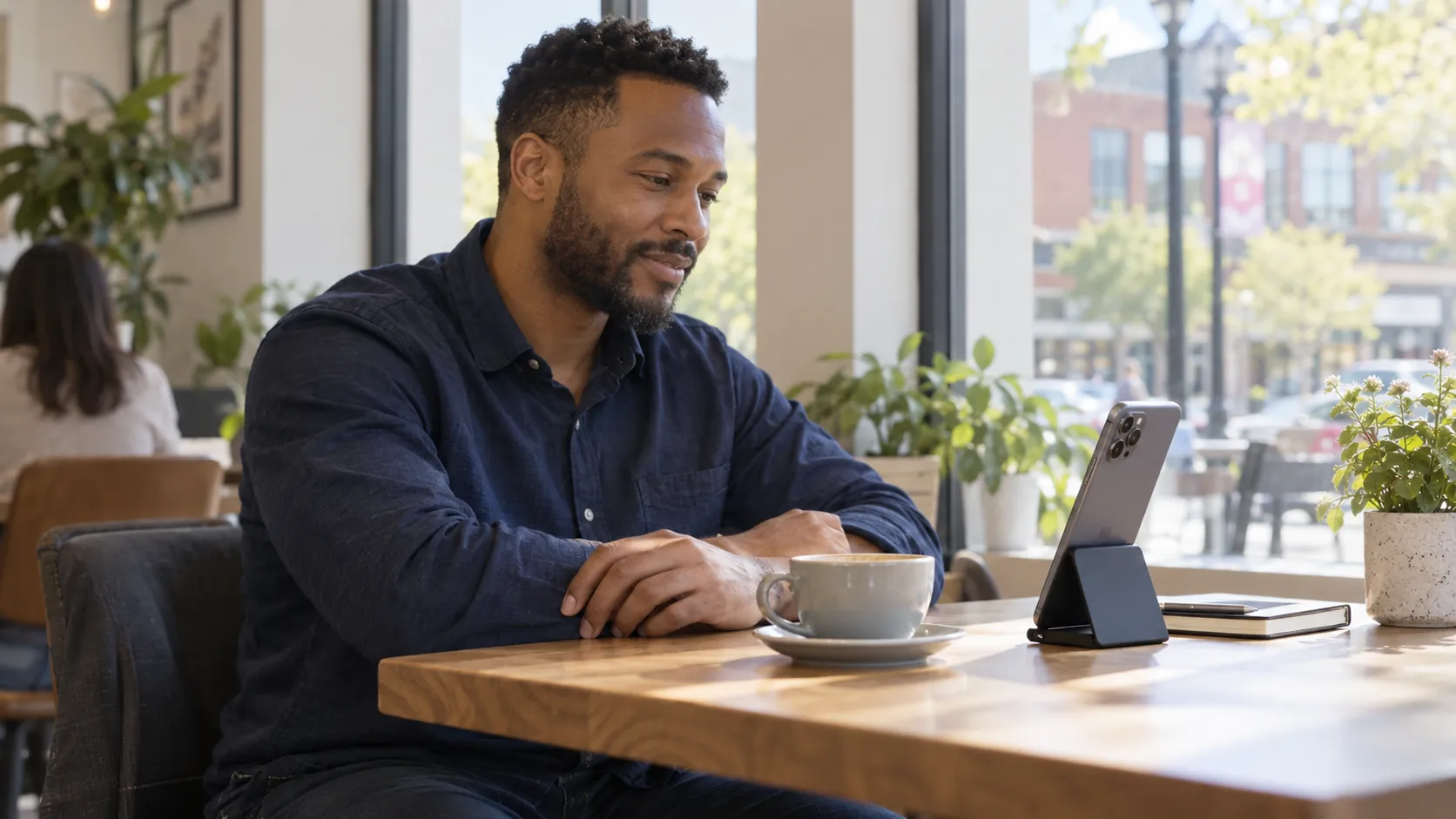 A man sitting at a cafe table with his smartphone on a stand and his forearms resting comfortably nearby.